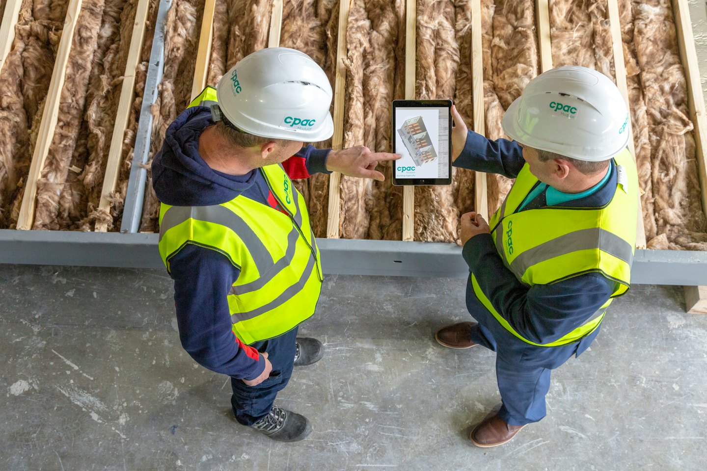 Dwóch budowlańców omawia tablet na placu budowy.